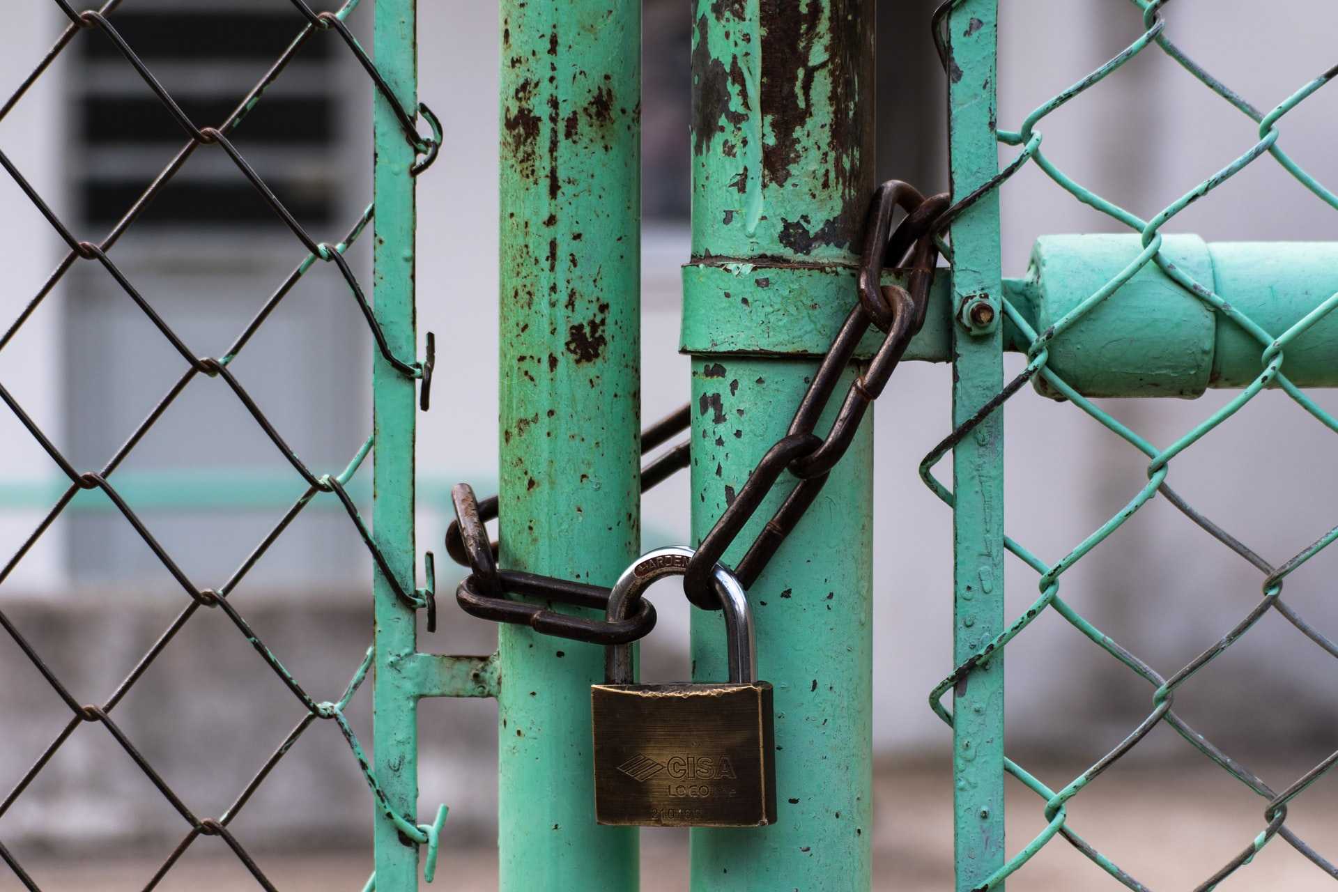 Padlock securing a chain on an aqua-coloured fence