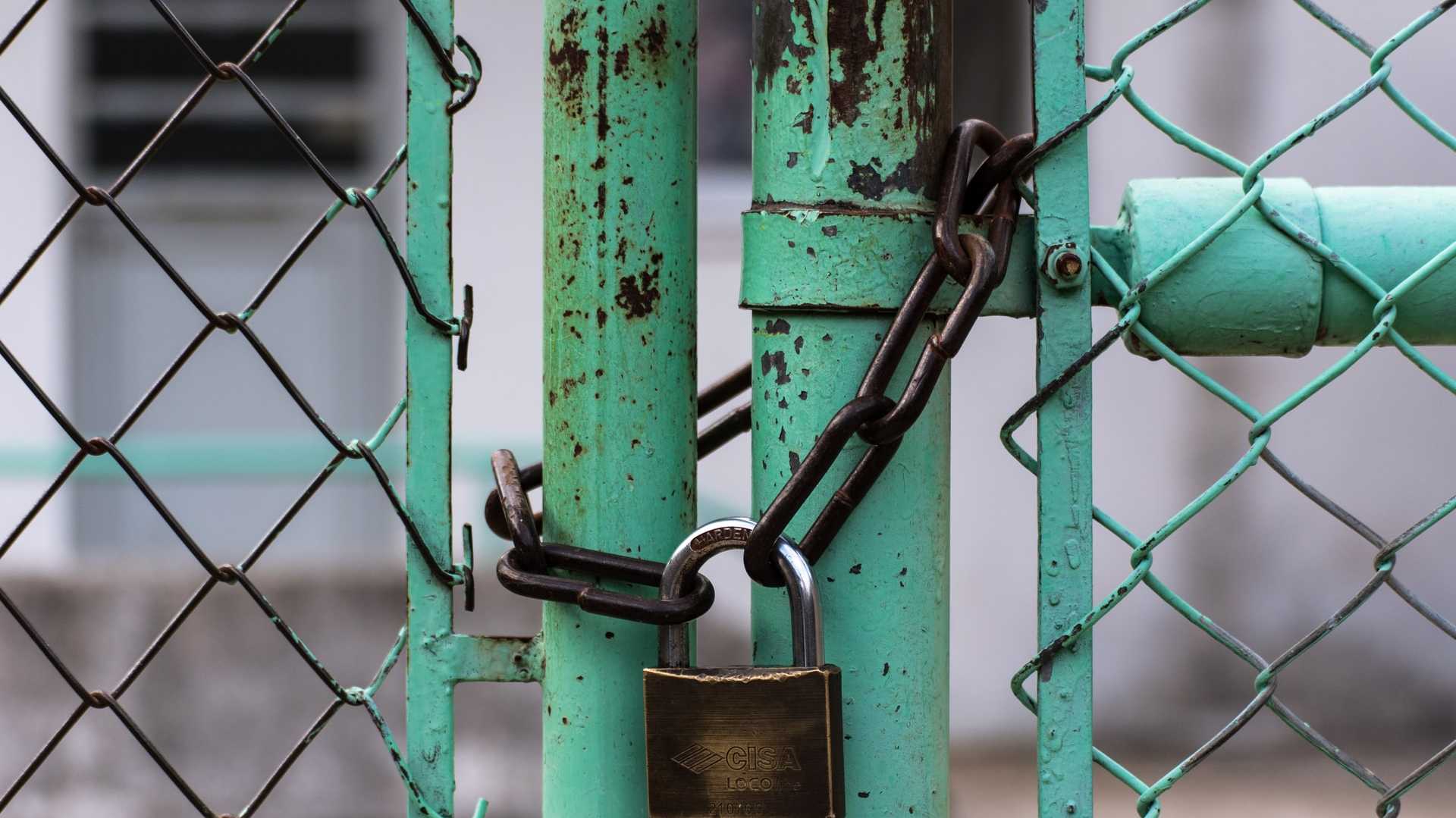 Padlock securing a chain on an aqua-coloured fence