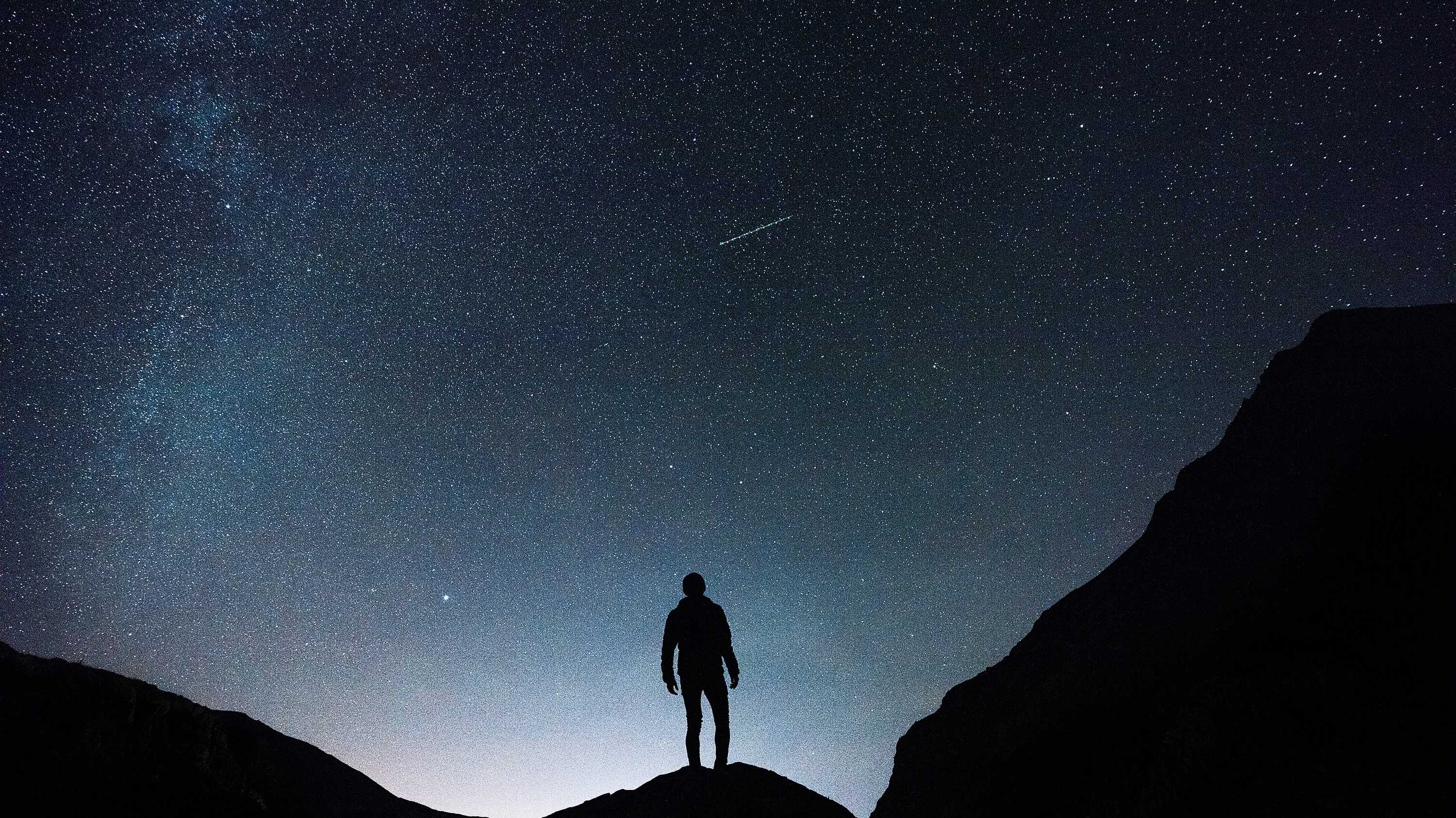 Silhouette of a man standing on a mountain looking at a starry night sky