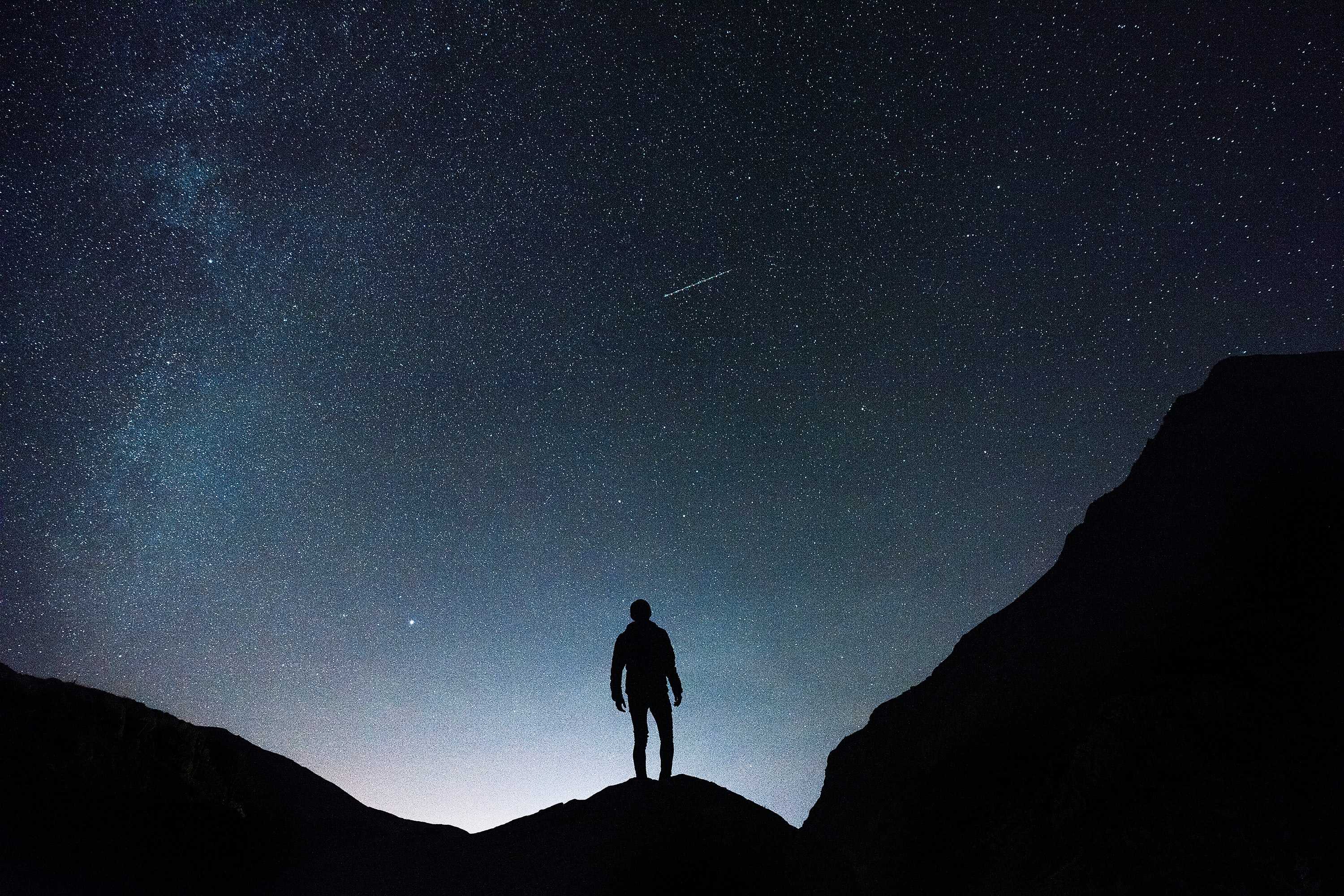 Silhouette of a man standing on a mountain looking at a starry night sky