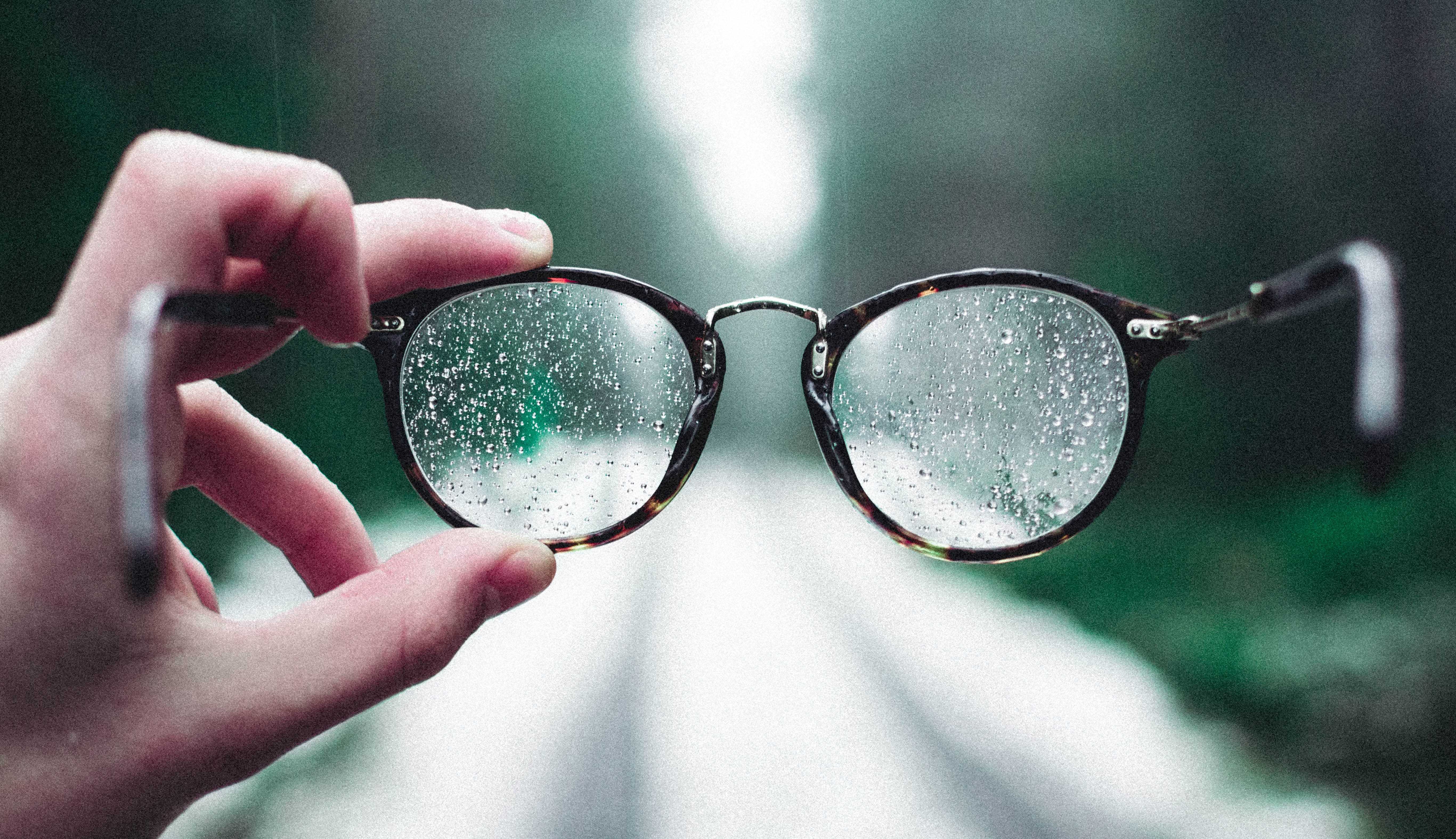 Person holding eyeglasses with water droplets