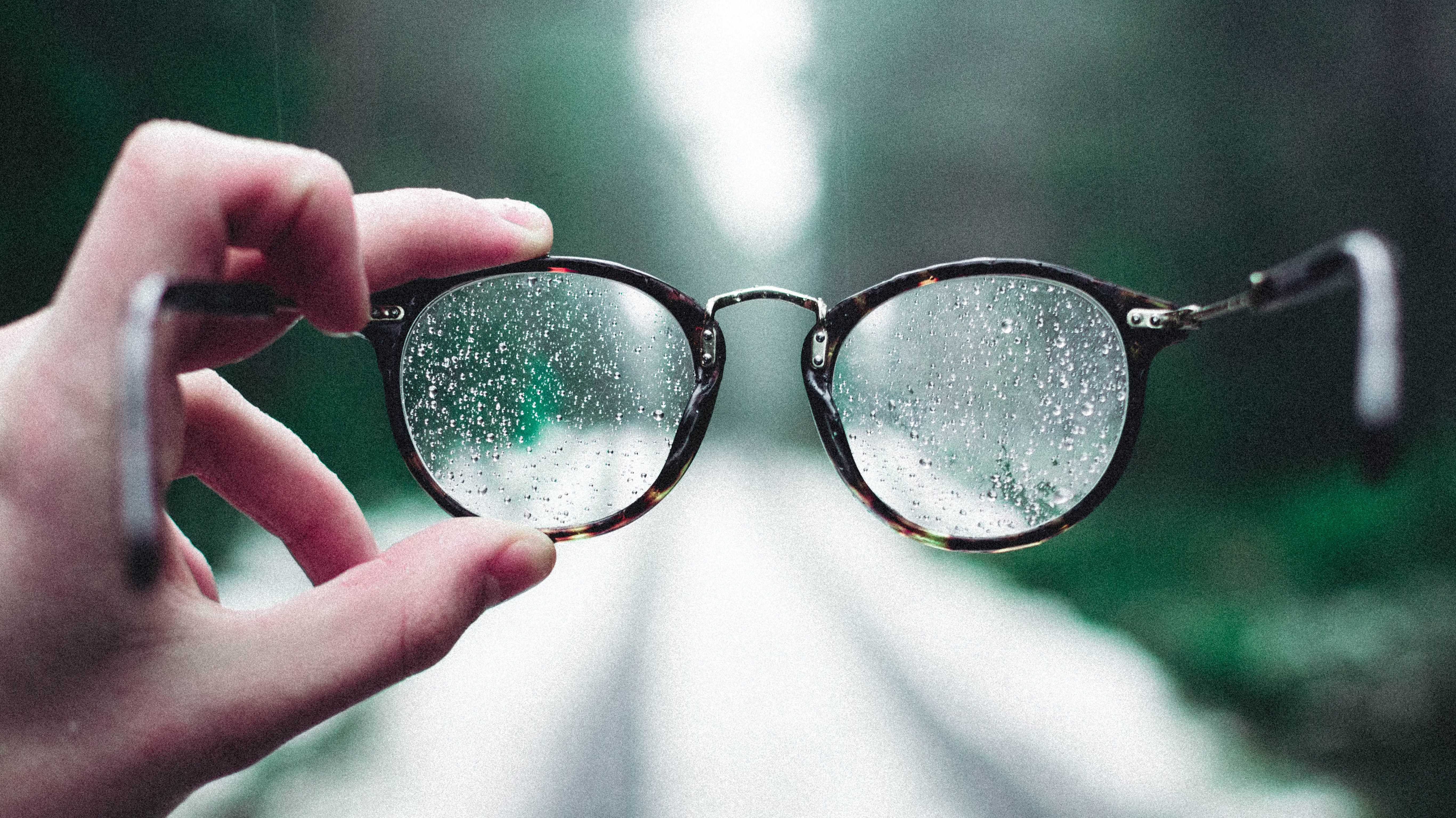 Person holding eyeglasses with water droplets